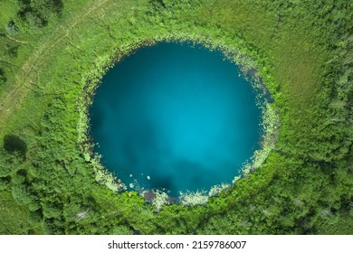 Aerial top down amazing lake of round shape. Cloudy sky reflected in clear turquoise water of pond surrounded by trees and plants. Ripple on water surface, windy sunny summer day.