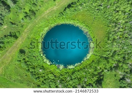 Aerial top down amazing lake of round shape. Cloudy sky reflected in clear turquoise water of pond surrounded by trees and plants. Ripple on water surface, windy sunny summer day