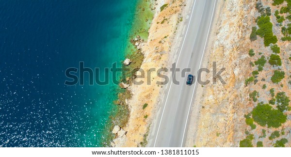 AERIAL, TOP DOWN: Car cruises down the empty asphalt\
road leading along the beautiful rocky beach in Lefkas. Flying\
above the coastline of an isle in the Mediterranean and car driving\
down scenic road
