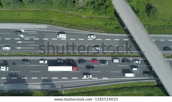 AERIAL, TOP DOWN: Cars and trucks drive through a\
congestion forming under the concrete overpass. Flying above the\
busy highway on a sunny day. Commuters and travelers driving up and\
down asphalt road