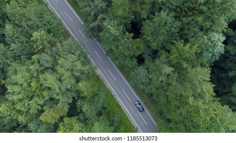AERIAL, TOP DOWN: Dark colored tourist car driving down empty asphalt road in the forest. Car on scenic cruise through the countryside drives along the empty route. Beautiful green nature of Slovenia.