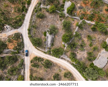 AERIAL, TOP DOWN: Dark SUV drives along a dirt track crossing the arid Mediterranean terrain of Murter island. Tourists on summer road trip cross the countryside filled with picturesque olive groves. - Powered by Shutterstock