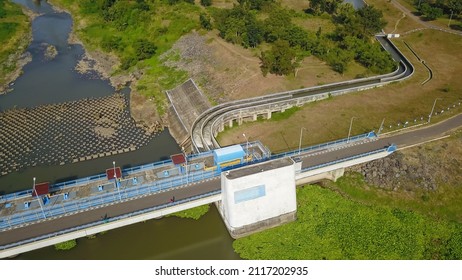 Aerial Top Down Drone Above Bendungan Sampean Baru In Java, Indonesia. Shot Over A Water Dam Reservoir With Asphalt Road Bridge Above Hydroelectric Ecology Renewable Energy With A Concrete Structure