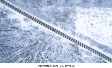 Aerial Top Down Drone Shot Of Snowy Forest Road With Red Car On It. Forest Road From Above