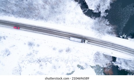 Aerial Top Down Drone Shot Of Snowy Road With Red Car And White Truck On It. Forest Road From Above