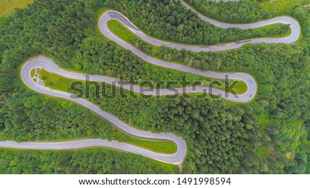 AERIAL, TOP DOWN: Motorcycles and cars driving on zig zag undulating road through lush dense spruce forest on mountain slope. Curvy switchback highway with hairpin turns snaking through the woods