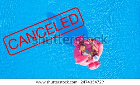 AERIAL, TOP DOWN: Spring break parties are all cancelled due to worldwide covid-19 quarantine. Relaxed young tourist couple chilling on a flamingo floatie toast with refreshing pineapple drinks.