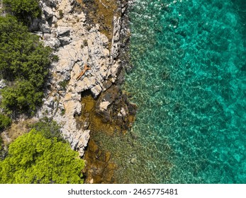 AERIAL, TOP DOWN: Unrecognizable young woman sunbathes and relaxes on a secluded shore on Murter island. Fit female tourist enjoys her summer vacation in Dalmatia by sunbathing in the Adriatic sun. - Powered by Shutterstock