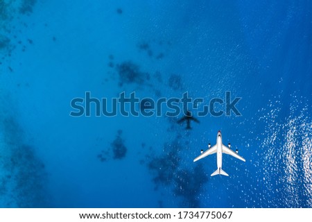 Aerial top down view of an airplane flying over blue sea as a travel concept with copy space