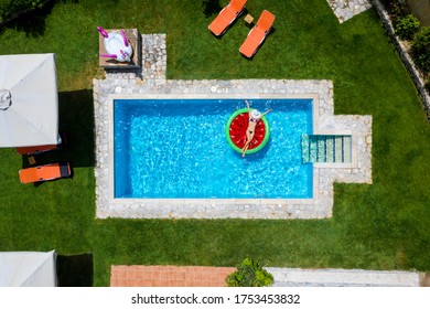 Aerial Top Down View Of An Attractive Woman In Bikini Floating On A Watermelon Shaped Float In A Pool Surounded By Green Grass