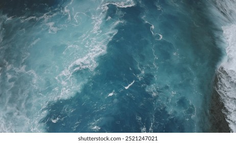 Aerial top down view blue ocean waves splashing foam. Dramatic deep water crashing sea coast. The stunning colors of the powerful storm high tide ocean surface seascape. Natural background. Drone shot