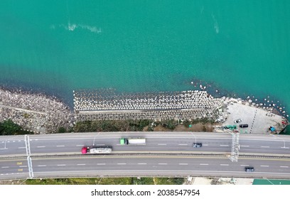 Aerial top down view of cars and trucks driving on a highway along the coast, which is protected with concrete tetrapods (dolosse), in Bali District, New Taipei City, Taiwan