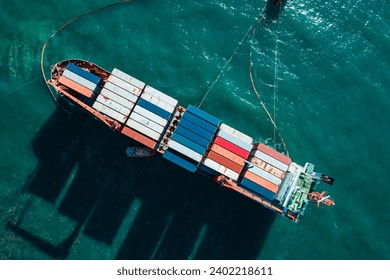 Aerial top down view of a container cargo ship stands aground after a storm with floating boom around the ship to prevent the spread of petroleum..