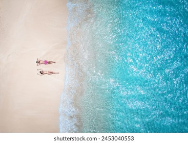 Aerial top down view of a couple in swimsuits sunbathing on a beautiful tropical beach in the Caribbean with turquoise sea - Powered by Shutterstock