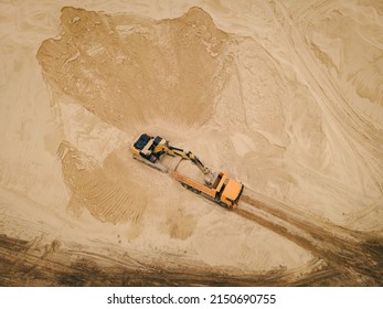 Aerial top down view of an excavator loading sand into a dump truck in opencast sand quarry