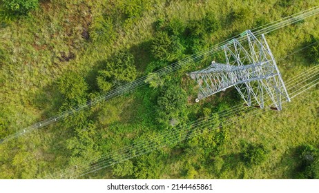 Aerial top down view high voltage steel power pylons in green field countryside. Flight over power transmission lines. Electric tower line, daylight, summer day.