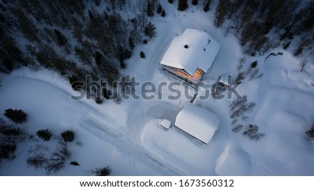 aerial top down view of a house covered in snow in the woods with cozy lights in the building