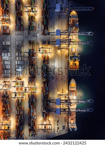 Aerial top down view of  large container cargo ship being unloaded by cranes and trucks in a commercial harbour during night time