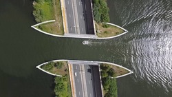 Aerial Top Down View Of Modern Aqueduct Or Water Bridge Is Constructed To Convey Watercourses Across Gaps Showing A Sailboat Moving Over The Infrastructure And Vehicles Cars Driving Under