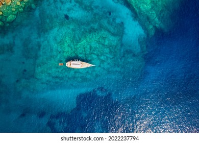 Aerial top down view of a sailing boat anchored on a emerald reef in the turquoise sea