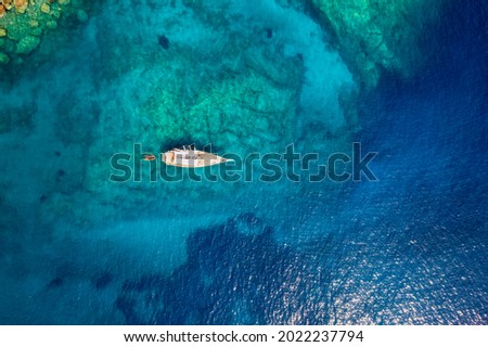 Aerial top down view of a sailing boat anchored on a emerald reef in the turquoise sea