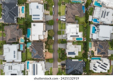 Aerial top down view of a suburban street lined with modern prestige homes with pools and rooftop solar in outer Sydney, Australia.
