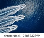 Aerial top down view of three motorboats cruising over the ocean with high speed