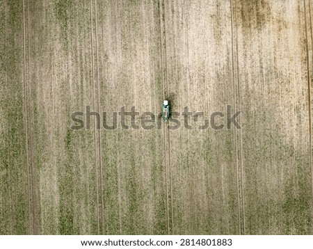 Aerial top down view of a tractor spraying pesticides or fertilizer on a green agricultural field with parallel tramlines.