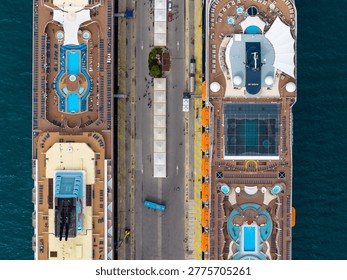 Aerial top down view of two luxury cruise ships docked at the port of Corfu, Greece. Highlighting swimming pools, sun loungers, and passengers on the top deck during a Mediterranean summer vacation
