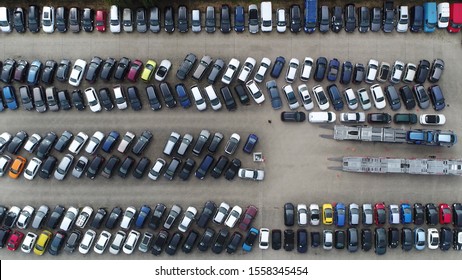 Aerial top down view of used car dealership lot showing parked vehicles and automobile offloaded from truck different colored roofs and all vehicle brands