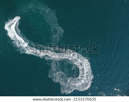Aerial top down view of water foam trace with nice deep blue shade of ocean. Beautiful white trail on the calm sea surface behind a small powerful motorboat. Propwash. Summer vacation travel concept