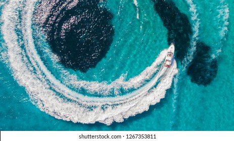 Aerial top down view of yacht racing across the flat Mediterranean turquoise water with white sands and clear blue sea.