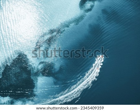 An aerial top shot of a boat leaving trail on clear seawater