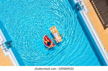 Aerial Top Vertical View Of People Old Senior Couple Enjoying The Retired Lifestyle Lay Down With Trendy Coloured Lilos Inflatable Mattress On A Blue Water Clear Swimming Pool In Resort Hotel Vacation