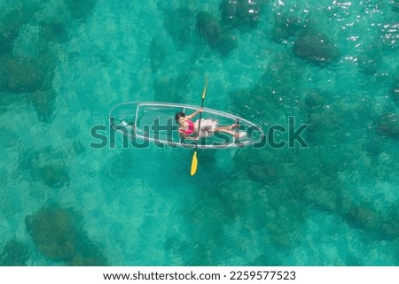 Aerial top view of Asian woman, a tourist, paddling a boat, canoe, kayak or surfboard with clear blue turquoise seawater, Andaman sea in Phuket island in summer season, Thailand. Water in ocean