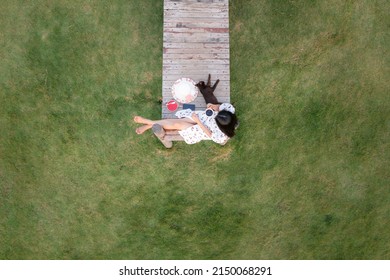 Aerial Top View Beautiful Asian Women And Cat Relaxing And Drinking Hot Coffee On The Wooden Bridge In The Garden Green Grass Background,