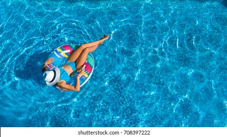 Aerial Top View Of Beautiful Girl In Swimming Pool From Above, Relax Swim On Inflatable Ring Donut And Has Fun In Water On Family Vacation
