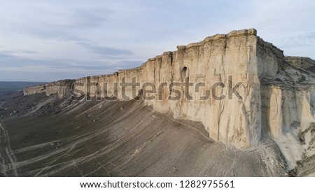 Aerial top view for breathtaking white cliff near green valley on beautiful, cloudy sky background. Shot. White, high rock cliff near the field with green grass.