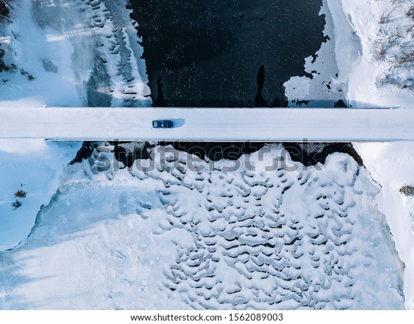 Aerial top view of bridge road above frozen\
river in snow winter Finland\
Lapland.
