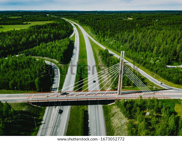 Aerial top view\
of cable-stayed Suspension bridge and Highway road with green\
forests on a summer day in\
Finland.