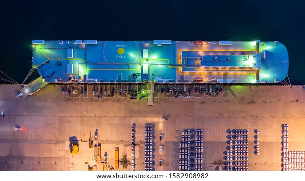 Aerial top view car carrier vessel at night, rows\
of new cars at night waiting to be dispatch and shipped import\
export new cars.