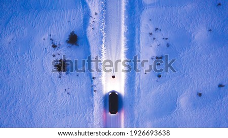 Aerial top view of car on rural area road while headlights are on in winter darkness, bird's eye view of suv vehicle in snowy north lands. Person standing front automobile which lighting the way