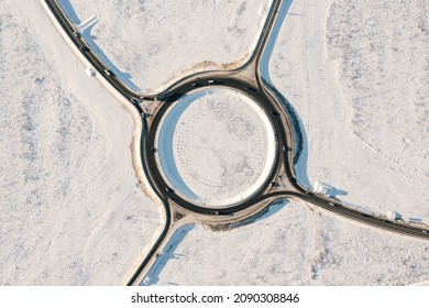 Aerial top view of circular traffic on winter road. Circle asphalt road with moving cars in sunny cold winter day. Car traffic on highway junction in winter season