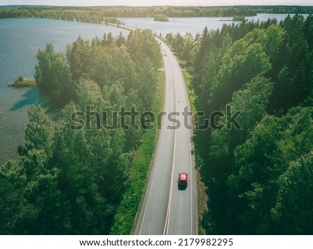 Aerial top view of country road through green woods and blue lakes in summer Finland