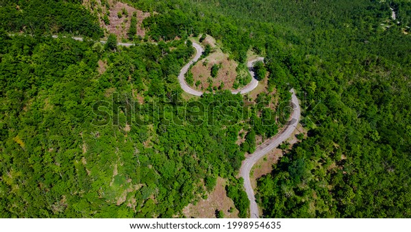 aerial top view of\
curves roadway pass through fresh green forest on mountain, road\
path uphill in urban