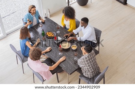 Aerial or top view of diverse friends or people wearing casual clothes, smiling with happiness, sitting at dining table, holding glass of wine, party celebration at cozy home. Event, New Year Concept