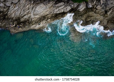 Aerial top view from drone of sea waves hitting rocks and small fishing man on island in Phuket, Thailand