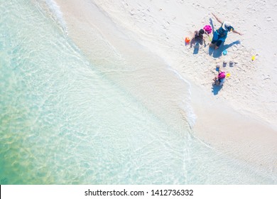 Aerial top view of happy young mum with children building a sandcastle together on tropical shore. Colorful turquoise sea. Peaceful andaman sea at Koh Lipe, Satun, Thailand.