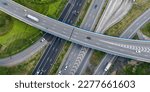 Aerial top view of highway junction interchange road. Drone view of the elevated road, traffic junctions, and green garden. Transport trucks and cars driving on highway. Infrastructure in modern city.