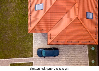 Aerial Top View Of House Metal Shingle Roof With Attic Windows And Black Car On Paved Yard.